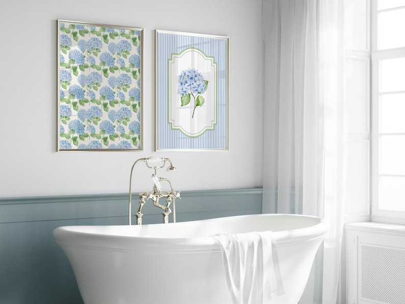 May include: Two framed floral art prints featuring blue hydrangea blooms. One print displays a pattern of hydrangeas, while the other showcases a single flower against a striped background. The prints are displayed above a white bathtub in a bathroom setting.
