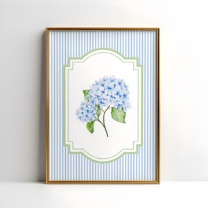 May include: A framed print with a watercolour illustration of blue hydrangea flowers and green leaves. The artwork is set against a white background within a green and white decorative border, and a blue and white striped background. The frame is gold.