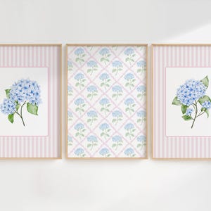 May include: Three framed floral prints. Two prints feature blue hydrangea blooms with green leaves on a white background, framed by pink and white striped borders. The center print has a repeating blue hydrangea pattern.