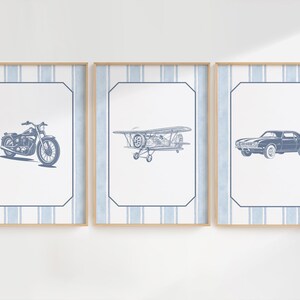May include: Three framed prints featuring vintage vehicles. The prints showcase a motorcycle, a biplane, and a classic car, all in a blue and white color scheme. Each print is set against a striped background and framed in light wood.