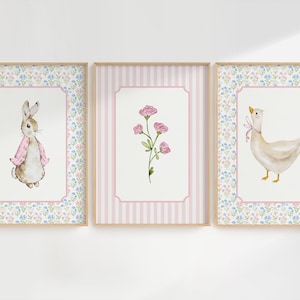 May include: Three framed watercolor prints. The first features a rabbit wearing a pink scarf, the second a pink flower, and the third a goose with a pink bow. Each print has a floral border and a light wood frame.