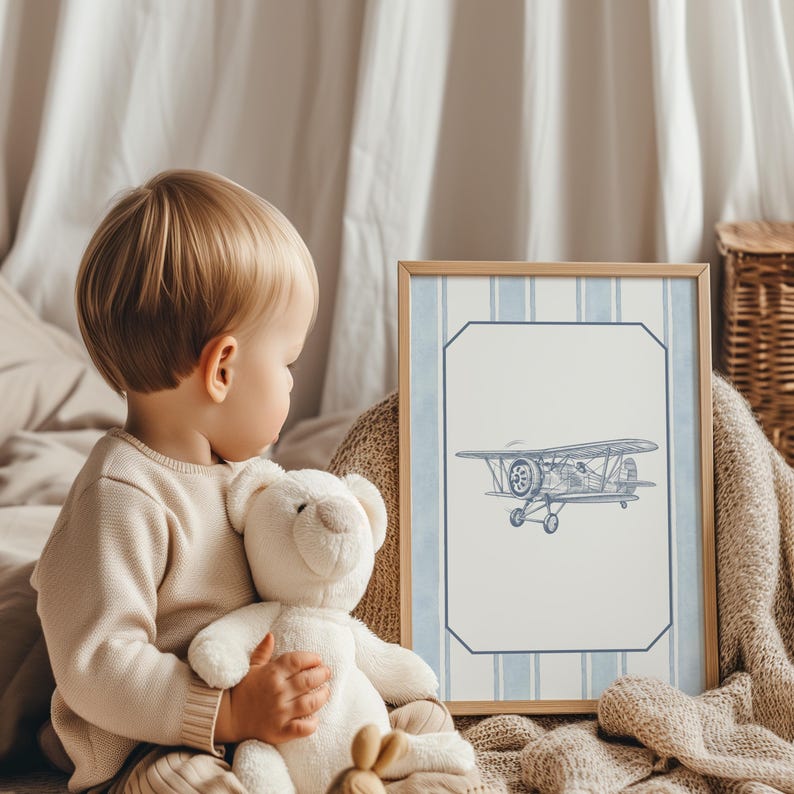 May include: A framed print featuring a blue and white biplane illustration. The artwork has a light wood frame and a blue striped border. The image is a children's room decor item.
