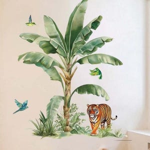 May include: A wall decal featuring a tropical scene with a large banana tree, a tiger, and several birds. The tree has large green leaves and a brown trunk. The tiger is orange and black. The birds are blue and green.