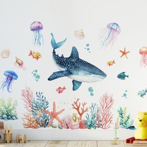 Pode incluir: Autocolantes de parede em aquarela com uma cena subaquática com um tubarão-baleia, águas-vivas, estrelas-do-mar e corais. O design inclui várias criaturas marinhas em tons de azul, rosa e laranja, criando um tema oceânico vibrante.