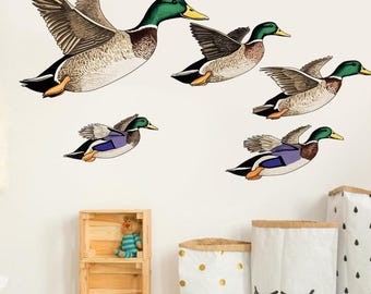 May include: Wall decals featuring five flying ducks. The ducks have green heads, yellow beaks, and brown and white bodies. The decals are designed to look like they are in flight, with their wings spread out. The background is white.