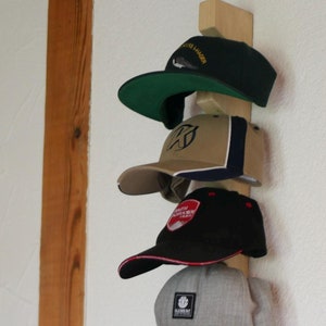 Könnte beinhalten: Ein hölzerner Hutständer mit acht Baseballkappen, die daran hängen. Die Kappen sind in verschiedenen Farben, darunter Grün, Beige, Schwarz, Grau, Braun, Marineblau und Rot. Einige der Kappen haben Logos oder Text darauf, wie "Joshua Tree National Park" und "Element".