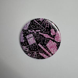 May include: A round button with a black background and a repeating pattern of white and pink objects, including a chair, guitar, and ladder. The button has a glossy finish and is set against a white background.