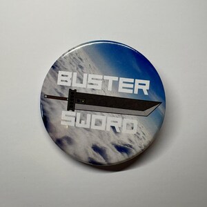 May include: A round button with a blue and white cloudy background. The button features the text "BUSTER SWORD" in white, with a black and gray sword graphic in the center. The button is a collectible item.