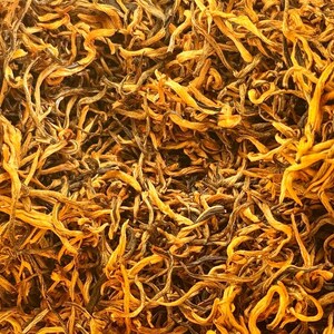 May include: Close-up of loose leaf black tea with golden tips. The tea leaves are long and thin, with a rich, dark brown color and a hint of gold.