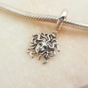 Pode incluir: Um berloque de prata com uma cabeça de Medusa detalhada com cabelo em forma de serpentes, suspenso numa pulseira de corrente de cobra de prata. O passador do berloque é acentuado com uma pequena pedra preciosa redonda e transparente.