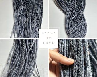 May include: A close-up of a bundle of gray and silver ombre synthetic dreadlocks. The dreadlocks are arranged in a loose braid and have a soft, textured appearance. The text "Locks of Love" is visible in the image.