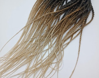 May include: A bundle of ombre synthetic hair extensions. The hair transitions from dark brown to light brown and then to a light blonde color. The hair is twisted into individual braids.