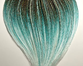 May include: A bundle of ombre synthetic hair extensions in shades of green, teal, and white. The hair is arranged in a heart shape.