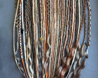 May include: A collection of handmade dreadlocks in various shades of brown, blonde, and orange. Some dreads are braided, others are wavy, and some are adorned with decorative beads and charms. The dreadlocks are arranged on a gray surface.