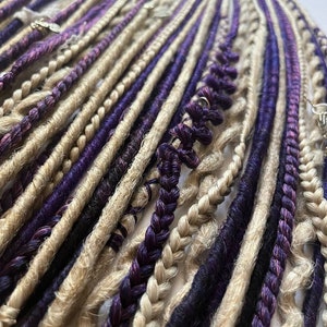 Puede incluir: Primer plano de un paquete de rastas sintéticas en tonos beige y morado. Las rastas están dispuestas en filas y están listas para ser instaladas.