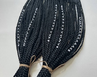 May include: A bundle of black braided hair extensions with white stitching. The extensions are tied together with twine.