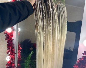 May include: A set of long, blonde and brown synthetic dreadlocks. The dreadlocks are arranged in a bundle and are hanging down.