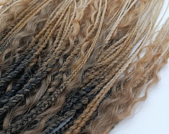 May include: Close-up of various shades of brown and black synthetic hair extensions. The extensions include braids and wavy strands, with a gradient effect from dark to light.