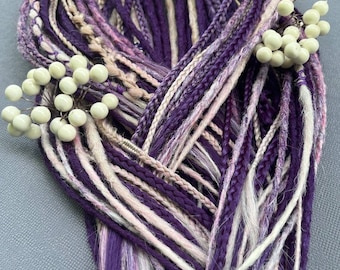 May include: A bundle of purple, lavender, and white dreadlocks, some braided, with a few sprigs of white berries. The dreadlocks are tied together at the top with twine. The color palette includes shades of purple, pink, and white.
