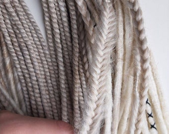 May include: A bundle of synthetic hair extensions in shades of white and light brown. The hair is braided and ready to be used for dreadlocks.