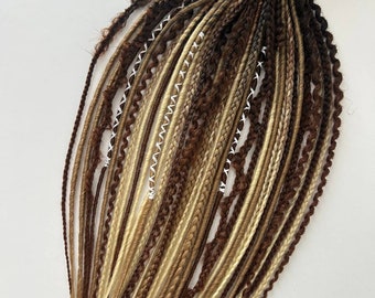 May include: A bundle of brown, blonde, and black synthetic dreadlocks and braids tied together with twine. The dreadlocks vary in thickness and texture, with some featuring white thread accents. The color palette includes shades of brown, blonde, and black.