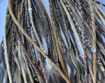 May include: A collection of handmade dreadlocks in various shades of brown, beige, and gray. Some dreads are adorned with decorative wraps, beads, and charms. A dark feather is also included in the arrangement, adding a natural element to the design.