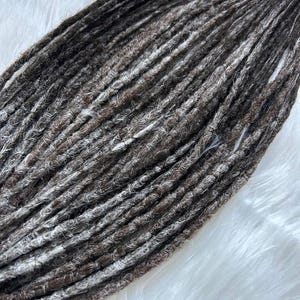 May include: A bundle of brown and white synthetic dreadlocks. The dreadlocks are long and thick, and they have a slightly textured appearance.