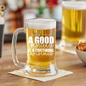 Può includere: Un boccale di birra trasparente pieno di birra e sormontato da schiuma bianca. Il boccale ha un manico e il testo "A GOOD CONSUME IS A CONTINUAL CHRISTMAS" in bianco. Un altro bicchiere di birra è sullo sfondo.