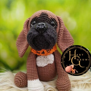 Puede incluir: Un juguete de perro de crochet marrón y negro con un collar blanco y un dije plateado que dice "hecho con amor".