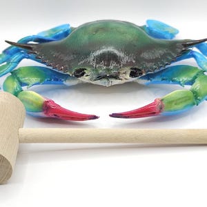 May include: A colorful crab sculpture with a green and blue shell, blue legs, and red claws. A wooden mallet is in the foreground. The crab is a decorative item.