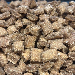 Puede incluir: Primer plano de un montón de pequeñas piezas cuadradas de cereal marrón.