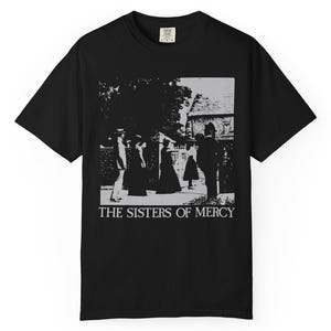 Könnte beinhalten: Ein schwarzes Kurzarm-T-Shirt mit einem weißen Grafikdruck, der eine Gruppe von Menschen vor einem Gebäude zeigt. Der Text THE SISTERS OF MERCY ist in weißen Großbuchstaben unter der Grafik auf der Vorderseite des Kleidungsstücks gedruckt.