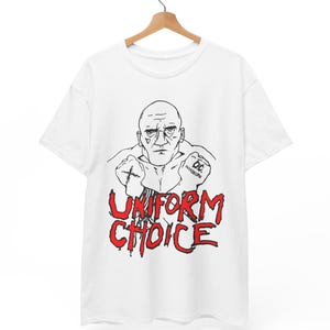 May include: White t-shirt featuring a black and red graphic. The graphic includes a stern-faced bald man with tattoos and the words "UNIFORM CHOICE" in red, dripping letters. The shirt is hanging on a wooden hanger.