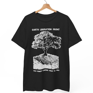 May include: Black t-shirt featuring a white tree graphic and the text "EARTH LIBERATION FRONT" above it. Below the tree is the text "YOU CANNOT CONTROL WHAT IS WILD". The t-shirt is displayed on a wooden hanger.