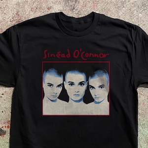 以下が含まれることがあります： シニード・オコナーのグラフィックが特徴の黒いTシャツ。デザインには、赤い枠の中に歌手の3つの肖像画が含まれており、その上に彼女の名前が赤いスクリプトで書かれています。肖像画は、彼女が丸刈りで中立的な表情をしている様子を示しています。