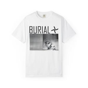 May include: A white short-sleeve t-shirt featuring the black text BURIAL above a black and white graphic illustration of a hooded figure. The design is centered on the chest of the garment, which has a crew neckline and a standard fit.