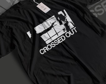 May include: A black short-sleeved t-shirt featuring a white graphic print of a person holding a firearm behind a window grid. The text CROSSED OUT is printed in white below the graphic. A white tag labeled LARGE is attached to the neckline.