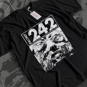 Op de afbeelding: Een zwart t-shirt met korte mouwen en een witte rechthoekige grafische print met de tekst FRONT 242 boven een contrastrijke, verweerde zwart-witafbeelding van een gezicht. Een wit label met maat L is aan de kraag bevestigd.