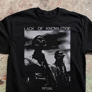 Könnte beinhalten: Schwarzes T-Shirt mit einer Grafik, die zwei Personen mit Gasmasken zeigt, mit dem Text "LACK OF KNOWLEDGE" darüber und "RITUAL" darunter. Das Bild ist in Schwarzweiß gehalten.