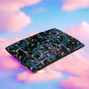 Può includere: Una pochette nera con cerniera con un motivo geometrico colorato che presenta lune crescenti e linee. La pochette è realizzata in un tessuto morbido e testurizzato.