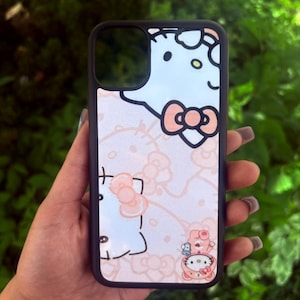 Puede incluir: Una funda de tel&eacute;fono negra con un dise&ntilde;o de Hello Kitty en azul claro y rosa. La funda tiene un borde negro y un patr&oacute;n repetido de la cara y los lazos de Hello Kitty. El dise&ntilde;o incluye una peque&ntilde;a ilustraci&oacute;n de Hello Kitty con un oso.