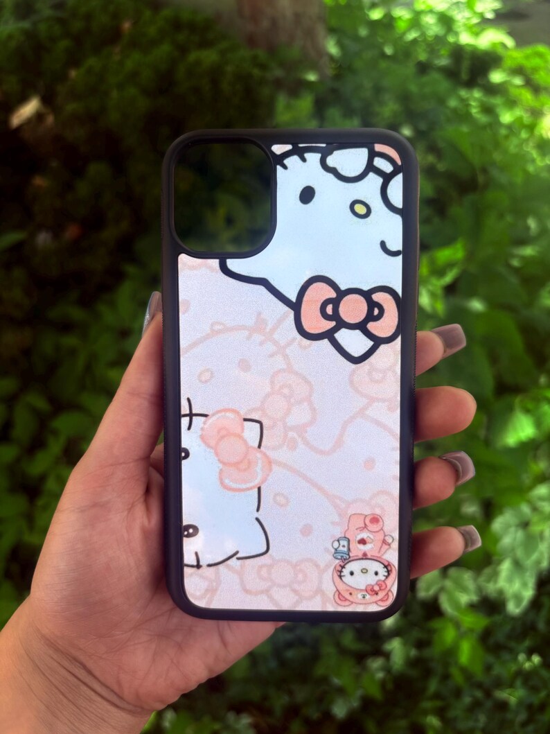 Puede incluir: Una funda de tel&eacute;fono negra con un dise&ntilde;o de Hello Kitty en azul claro y rosa. La funda tiene un borde negro y un patr&oacute;n repetido de la cara y los lazos de Hello Kitty. El dise&ntilde;o incluye una peque&ntilde;a ilustraci&oacute;n de Hello Kitty con un oso.