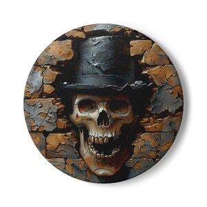 May include: Circular decorative item depicting a skull in a black top hat, breaking through a weathered brick wall. The skull has detailed teeth and is painted in shades of brown and beige. The brick wall is a mix of brown, grey, and beige.