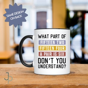 Op de afbeelding: Witte keramische koffiemok met een zwarte rand en handvat. De mok heeft een humoristische spreuk in zwarte tekst erop gedrukt: "What part of fifteen two fifteen four a pair is six don't you understand?"