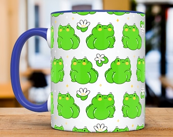 May include: White ceramic mug with a blue handle. The mug features a repeating pattern of green frogs with white flowers and gold glitter.