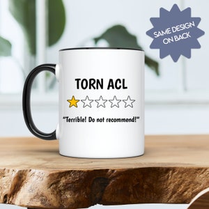May include: White coffee mug with a black rim and handle. The mug features a black and white graphic of a one-star rating with the text "Torn ACL" and "Terrible! Do not recommend!"