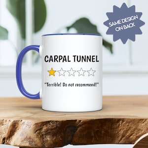 May include: White coffee mug with a blue rim and handle. The mug has a black and white graphic of a one-star rating with the text "CARPAL TUNNEL" and "Terrible! Do not recommend!"