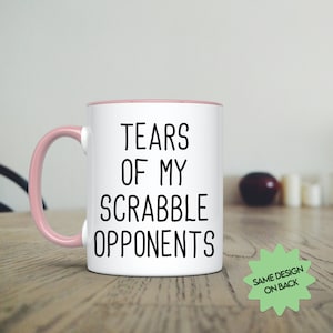 May include: White ceramic mug with a pink rim and handle. The mug has black text that reads "Tears of my Scrabble Opponents".