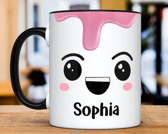 Könnte beinhalten: Weiße Keramiktasse mit schwarzem Henkel. Die Tasse hat einen pinkfarbenen, tropfenden Überzug und ein Comic-Gesicht mit schwarzen Augen, einem schwarzen Lächeln und rosa Wangen. Der Name "Sophia" ist in Schwarz unter dem Gesicht geschrieben.