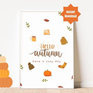 Könnte beinhalten: Ein druckbarer Wandkunstdruck mit weißem Hintergrund und braunem Text, der "Hello autumn. Have a cozy day." lautet. Der Druck zeigt Illustrationen von einem Kürbis, einer Tasse heißer Schokolade, einem Pullover, einem Hut, einem Paar Socken und Blättern.